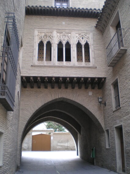 An arched passageway with a tiled roof and a building with a decorative window. 2