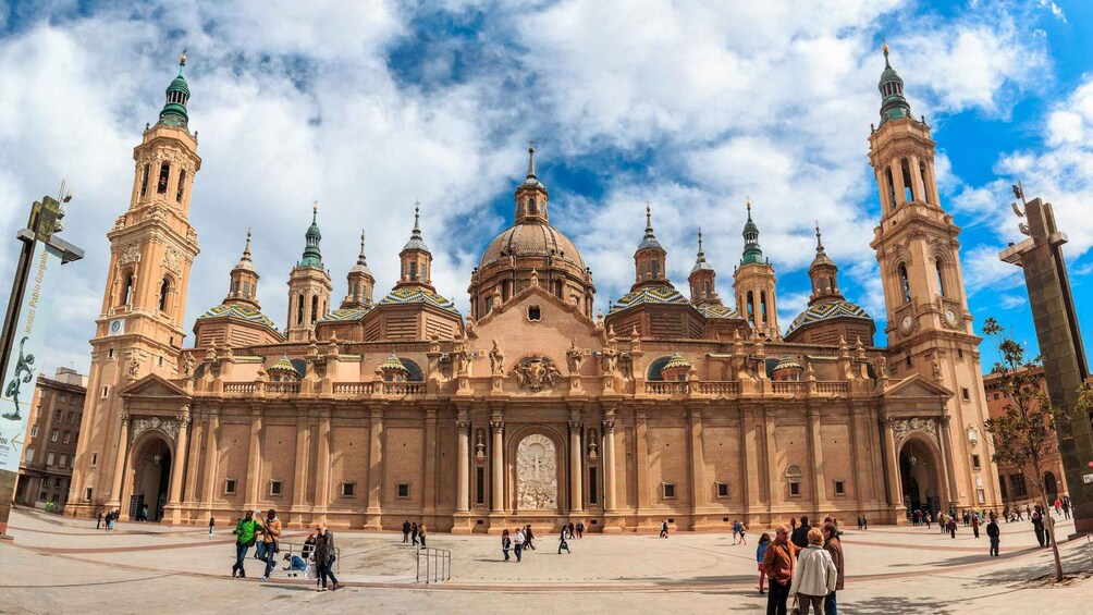 A large historic building with multiple domes and towers, surrounded by a plaza with people. 3