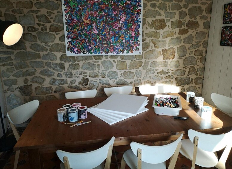 A rustic stone wall, a wooden table with art supplies, and a colorful abstract painting. 1