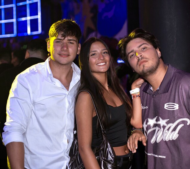 Three people posing together at an event with a stage and blue lighting in the background. 3