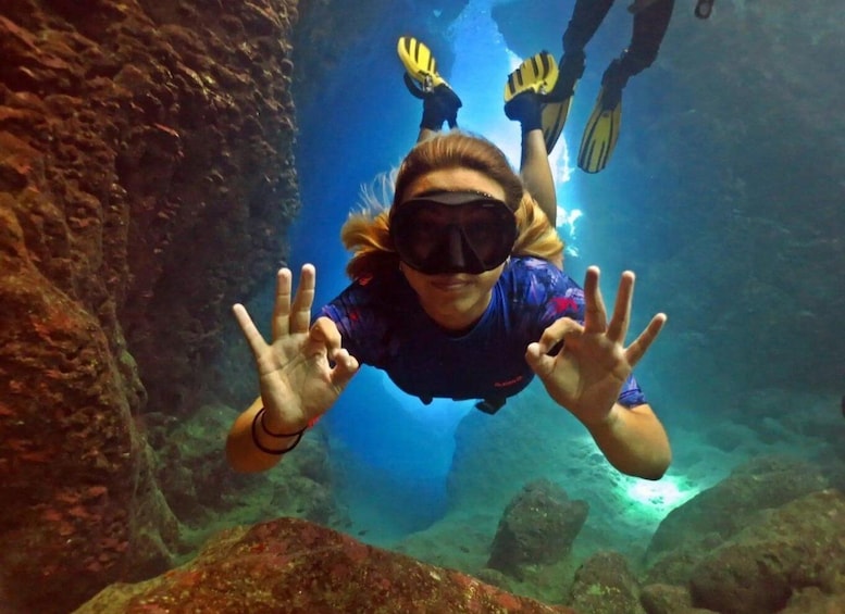 A person scuba diving underwater, surrounded by rocks and clear water. 2