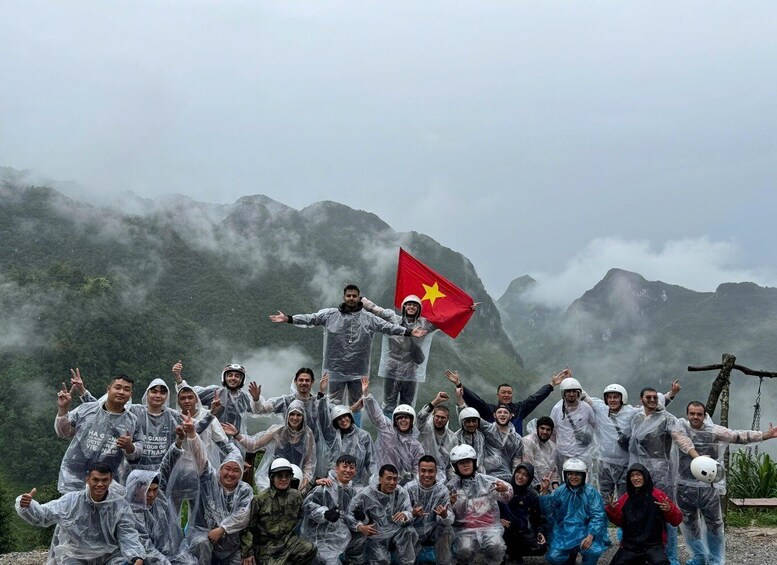 A group of people in rain gear posing with a flag, surrounded by misty mountains. 1