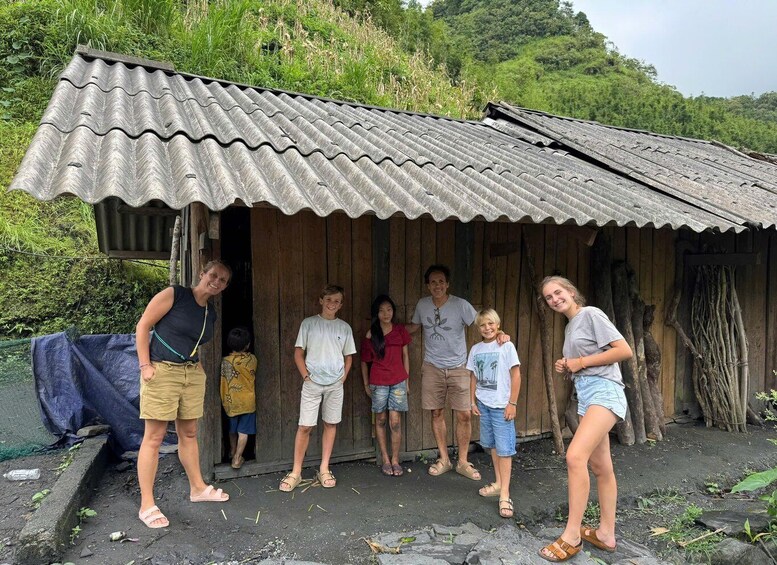 A group of people standing in front of a rustic wooden hut with a corrugated metal roof. 5