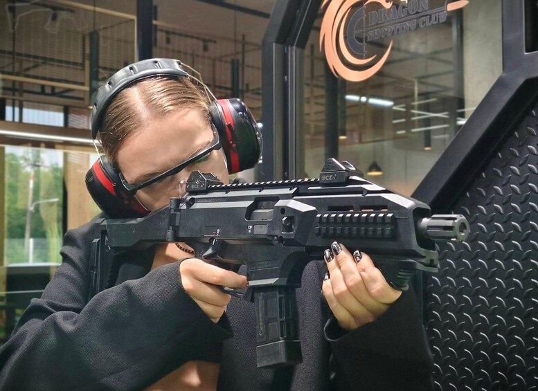 A person aiming a firearm indoors with a logo in the background. 1