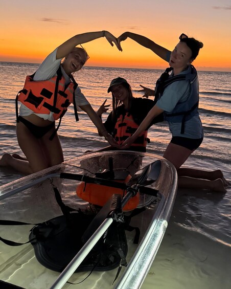 Three people on a boat at sunset with life jackets, a paddleboard, and a small motorized boat. 3