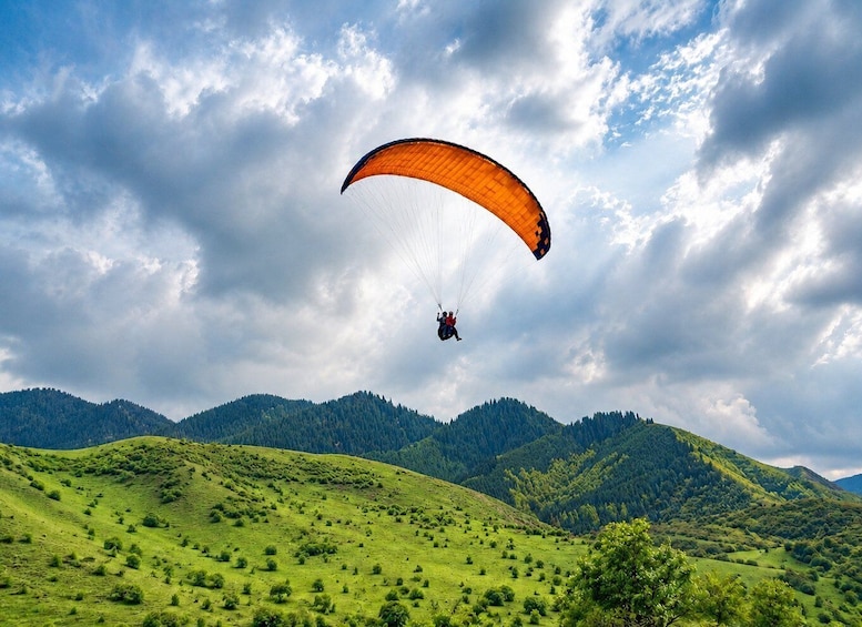 A paraglider flying over a green valley with hills in the background. 4