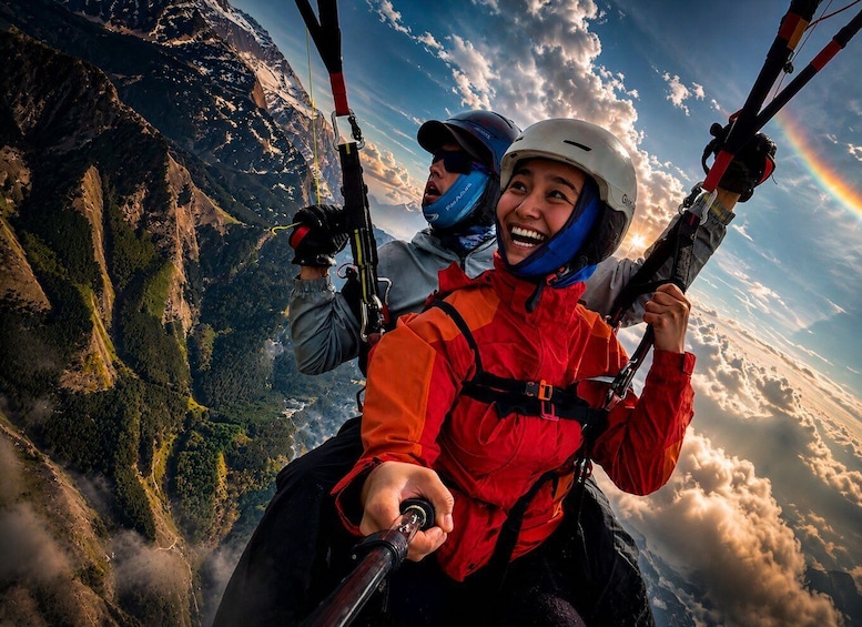 Two individuals paragliding over a mountainous landscape with a rainbow. 1
