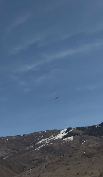 A person paragliding over a mountainous landscape with sparse vegetation and patches of snow. 2