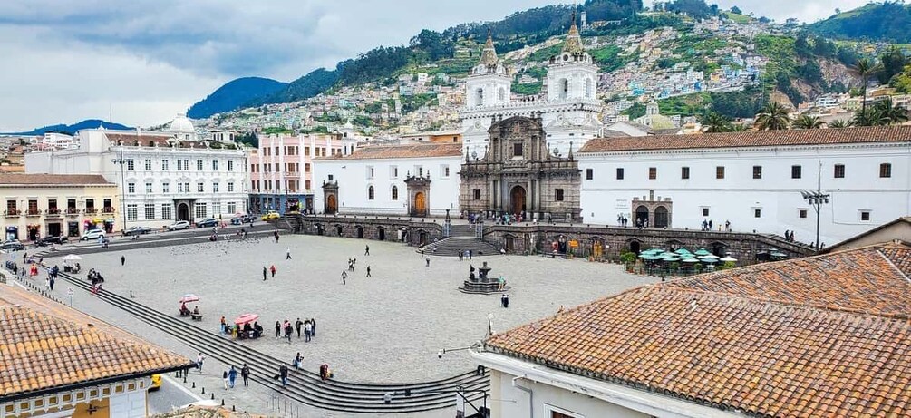 A plaza with a historic church, a large open square, and a hillside with buildings. 1