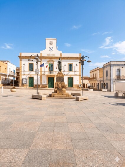 A town square with a central monument, a town hall building, and European flags. 2