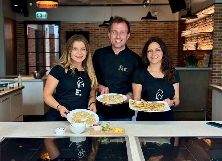 Three people in a kitchen holding plates of food, with a brick wall and modern appliances in the background. 1