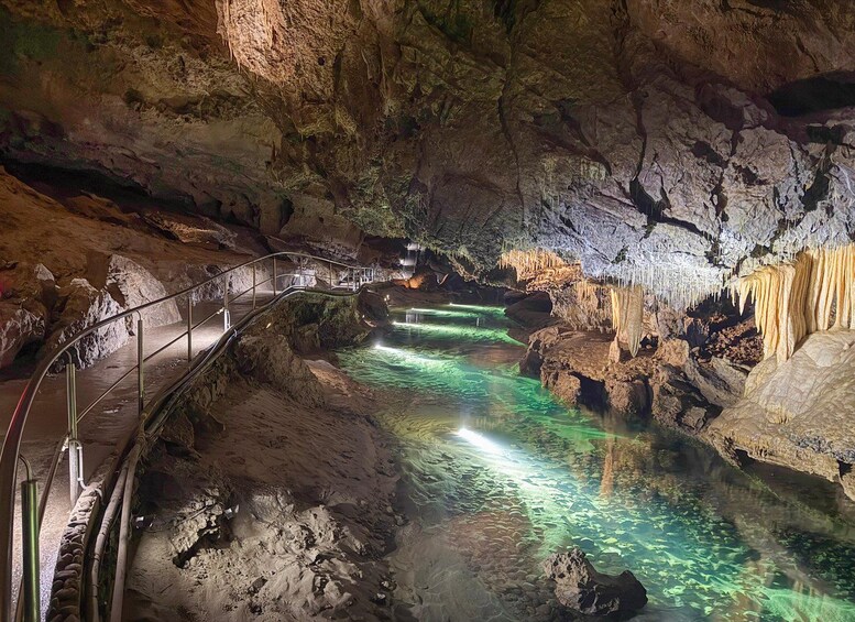 A cave with stalactites and stalagmites, a water stream, and a metal walkway. 3