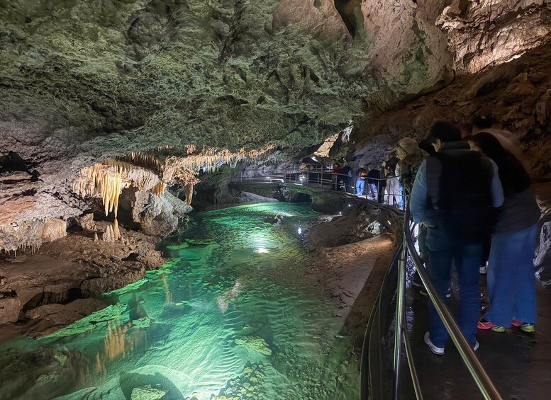A cave with stalactites, a water stream, and people observing. 4