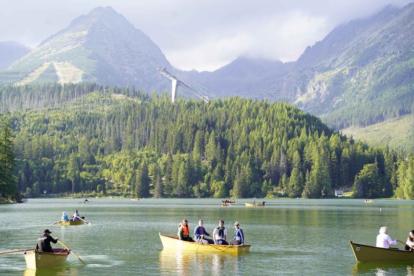 A group of people in a yellow boat on a lake surrounded by dense forests and mountains. 3