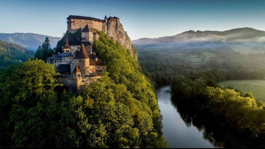 A castle perched on a cliff overlooking a river, surrounded by dense forest and hills. 3