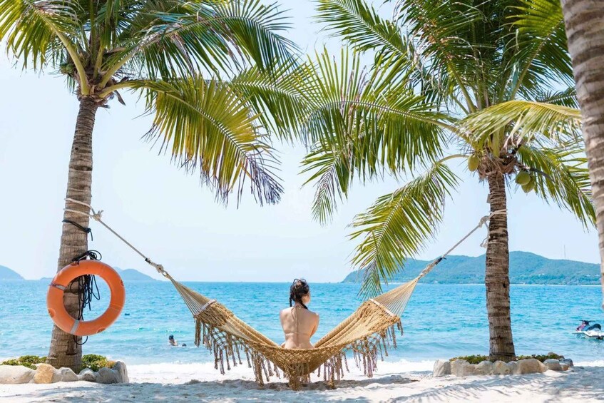 A hammock between palm trees on a beach with clear blue water and distant mountains. 1
