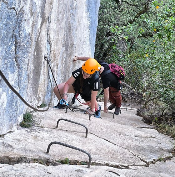 Two people climbing a rocky path with safety ropes and helmets. 3