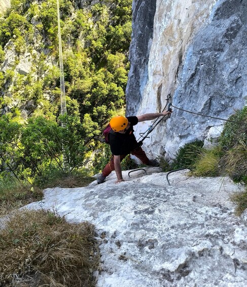 A person climbing a rocky cliff with a safety harness and a rope. 2
