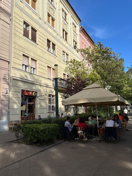 A café with outdoor seating, a building with ornate architecture, and a clear blue sky. 4