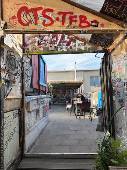 A narrow alley with graffiti-covered walls, a blue door, and a small outdoor seating area. 3
