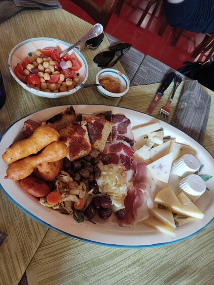 A plate of assorted foods including bread, cheese, olives, and meats, with a bowl of beans and tomatoes in the background. 4
