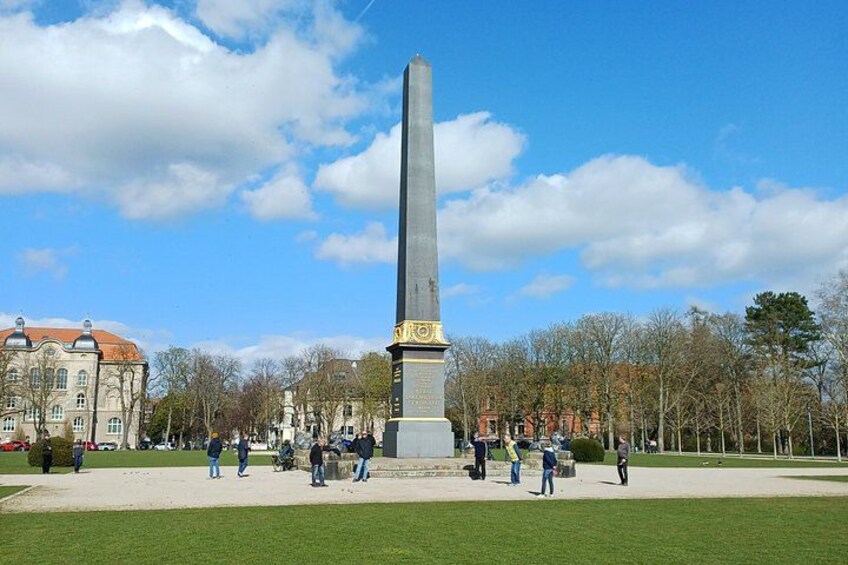 A tall monument with inscriptions, surrounded by a grassy area and trees. 4