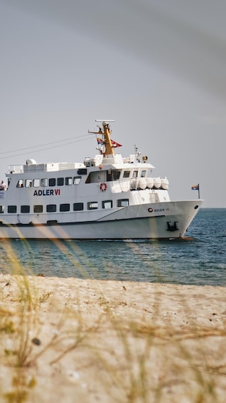 A white boat named 'ADLER VI' on the water with a flag on top and a lifebuoy on the side. 1
