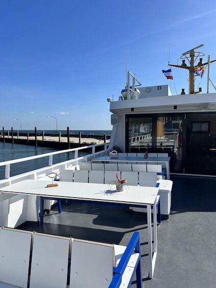 A boat deck with white tables and blue benches, a flagpole with flags, and a clear blue sky. 2