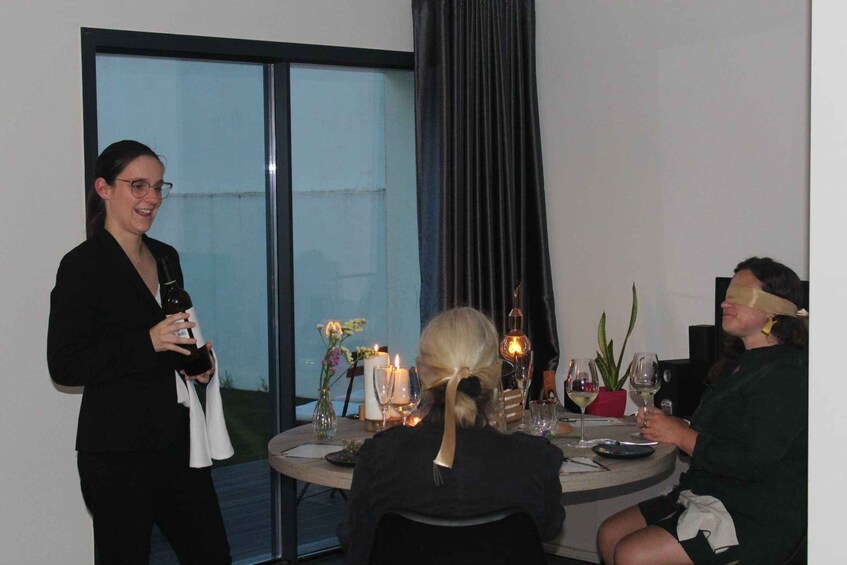 A person holding a bottle, a table with candles, and a glass of wine. 1