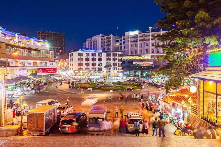 A busy urban square with a central monument, surrounded by brightly lit buildings and shops. 2