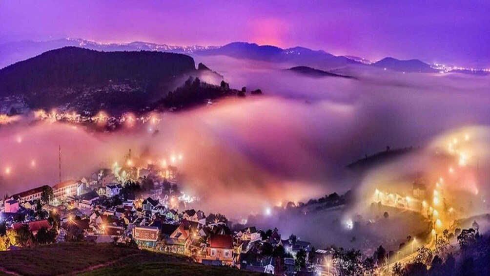 A town nestled in a valley with mountains in the background and a purple sky. 1