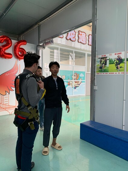 Two people in a room with a large number '26' balloon, a blue bench, and posters on the wall. 4
