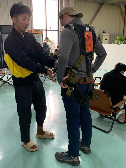 Two people in a room with a large window, one wearing a safety harness. 2