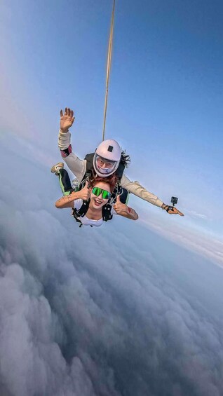 A person skydiving with a parachute above clouds. 1