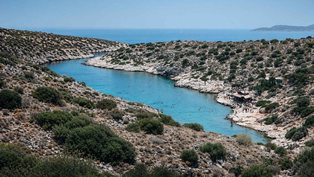 A coastal landscape with a rocky bay, clear blue water, and sparse vegetation. 4