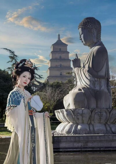 A person in traditional attire standing in front of a Buddha statue and a pagoda. 3