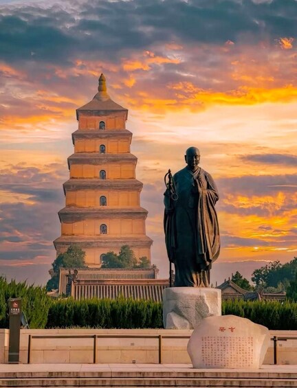 A pagoda with a statue in front, set against a sunset sky. 1