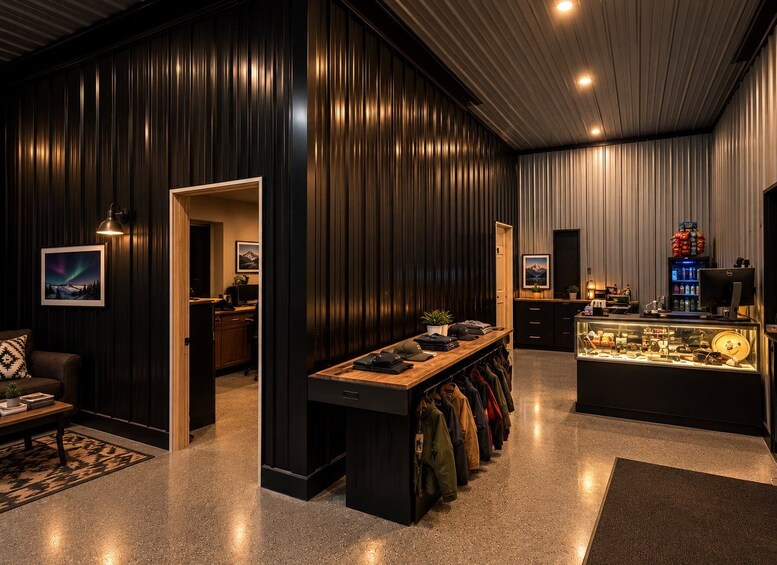 A modern interior with dark wood paneling, a wooden desk with a laptop, a coat rack, and a display case with various items. 2