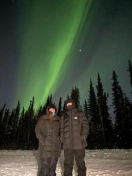 Two people standing in a snowy landscape with a green aurora in the sky. 3