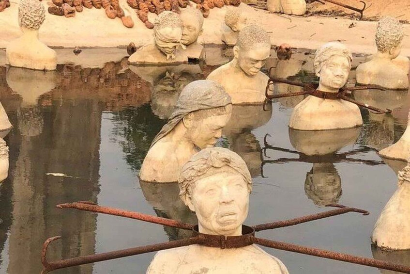 A collection of stone busts in a body of water, some with crossed sticks over their shoulders. 1