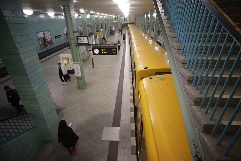 A subway station with a yellow train, tiled walls, and a staircase. 2