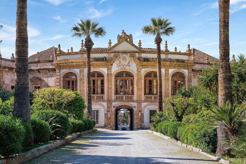 A historic building with a central archway, flanked by palm trees and surrounded by well-maintained gardens. 2