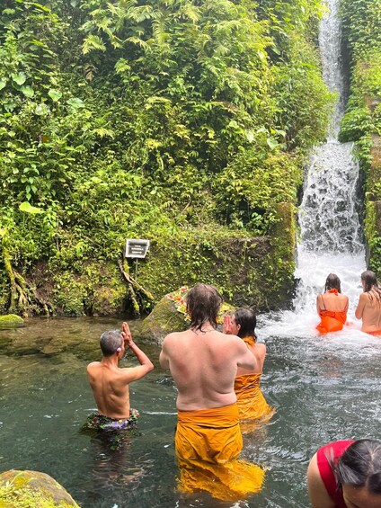 A waterfall surrounded by lush greenery, with people in traditional attire bathing in the water. 3