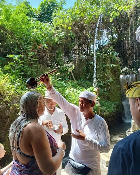 A group of people in a lush, green outdoor setting with a waterfall in the background. 1