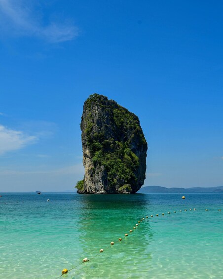 A clear blue sky, a large rock formation surrounded by turquoise water, and a distant shoreline. 4