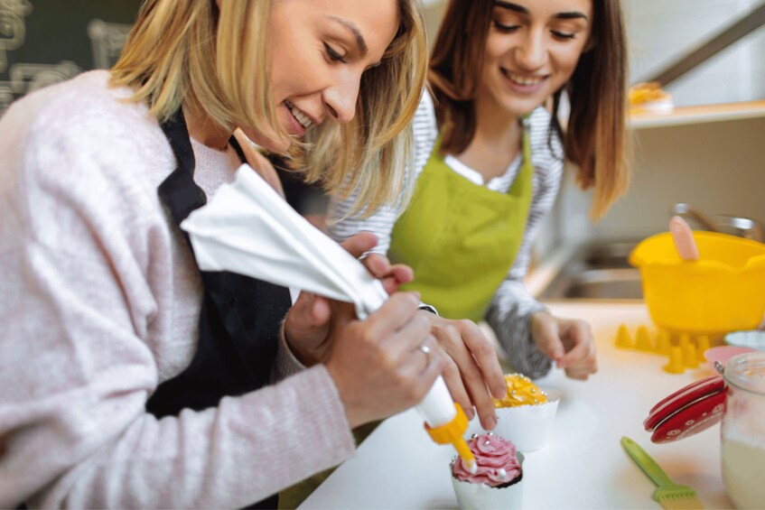 Two people decorating cupcakes with frosting. 1
