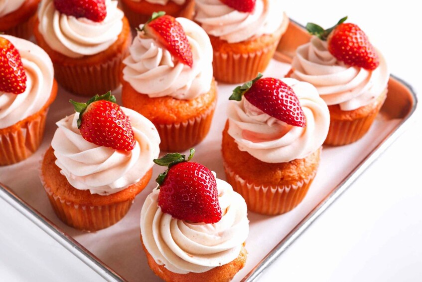 A tray of cupcakes with white frosting and strawberries on top. 4