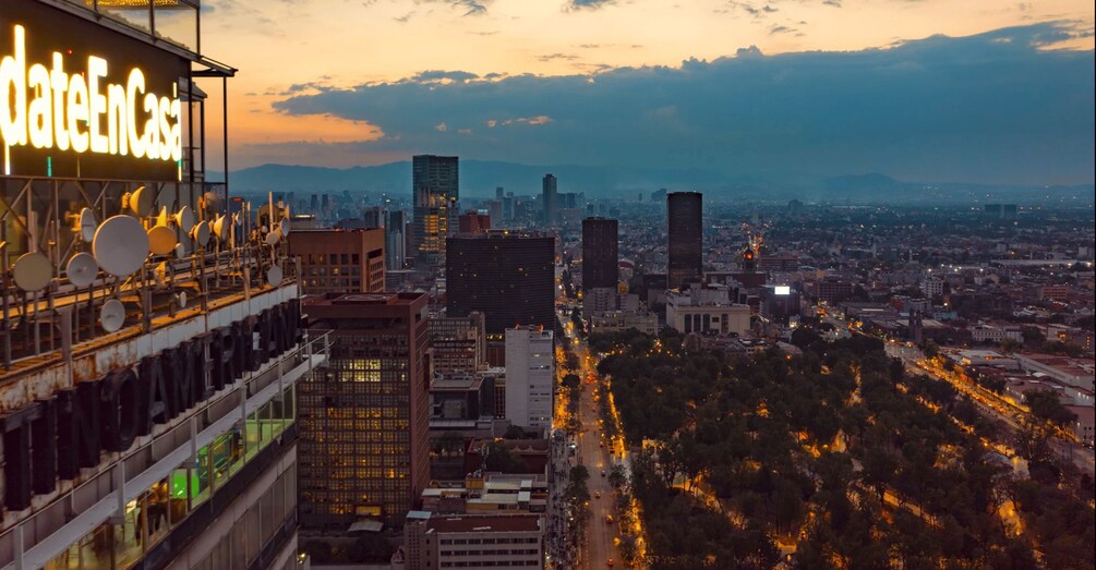 A cityscape at dusk with illuminated buildings and a prominent sign reading 'dateEnCasa'. 2