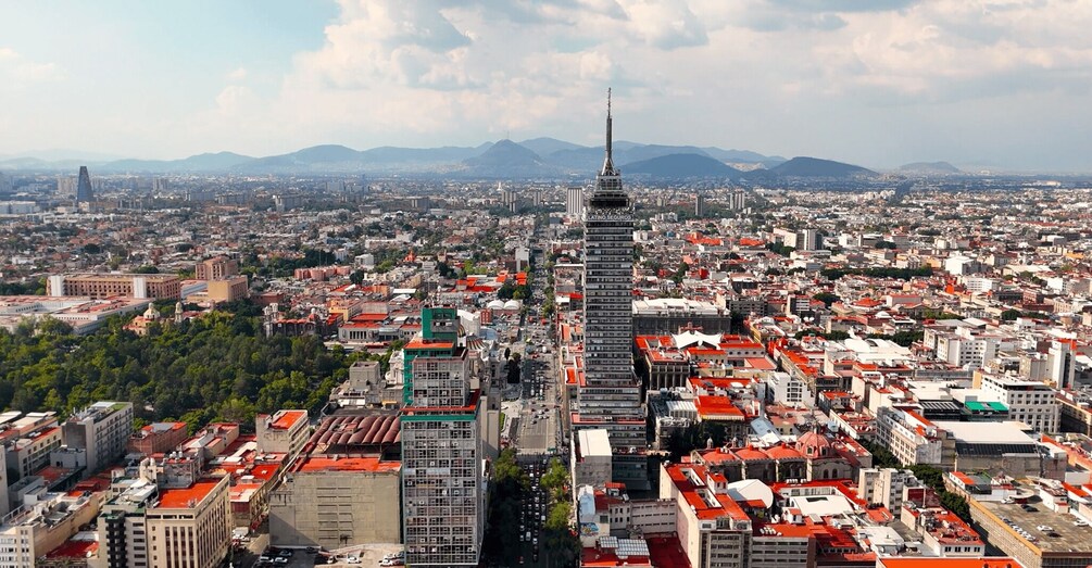 A cityscape with a prominent tower, dense urban buildings, and a mountainous backdrop. 3