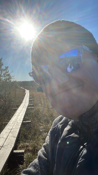 A person standing on a wooden boardwalk with a clear sky and sunlight in the background. 3